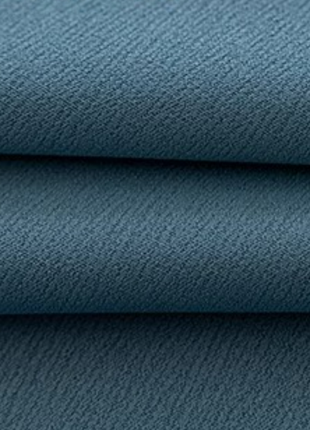 a close-up view of a textured fabric, possibly a piece of clothing or a textile. The fabric appears to be a dark blue color, with a slightly wrinkled and crumpled appearance.