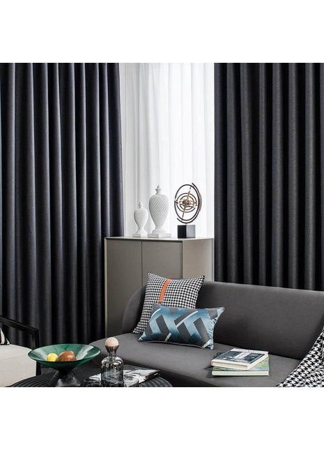 ein Wohnzimmer mit grauem Sofa und schwarzen Vorhängen