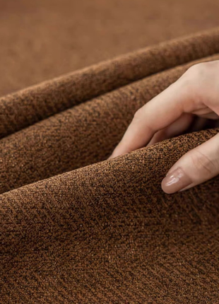 A hand is holding a piece of brown fabric, possibly a textile, and examining it closely.