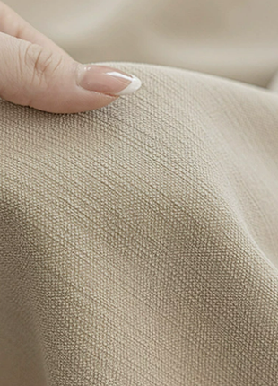 A close-up view of a hand resting on a beige fabric, with the fingers gently curled around the fabric.