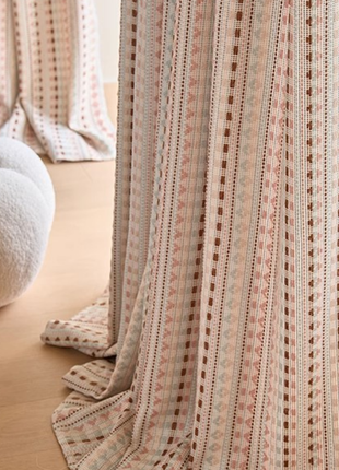 a close-up view of a curtain with a striped pattern in shades of pink and white. The curtain is partially drawn, revealing a wooden floor beneath it.