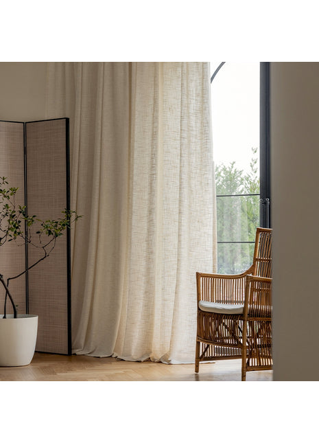 Ein Stuhl steht neben einem Fenster mit einem weißen Vorhang.