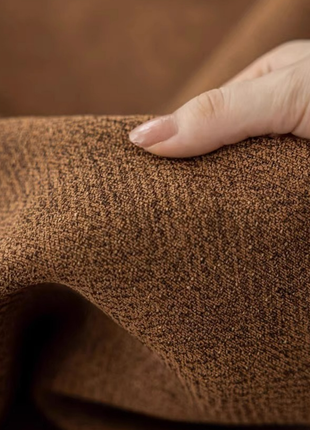 A close-up view of a hand resting on a textured brown fabric, with the fingers gently touching the surface.