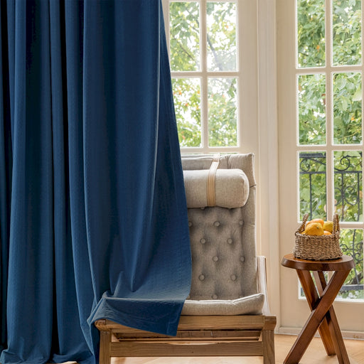 Ein Stuhl steht vor einem Fenster mit einem blauen Vorhang.