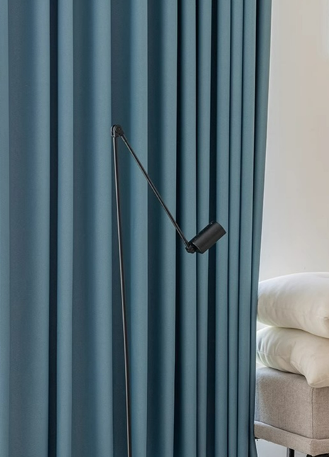 a modern living room with a blue curtain and a black floor lamp with a curved arm.