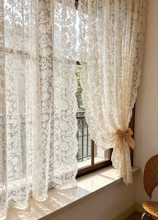 Voilage à broderie florale devant une porte-fenêtre de balcon, panneau retenu par un nœud beige